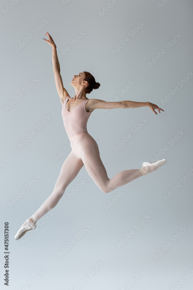 full length of graceful ballerina in bodysuit levitating and gesturing on grey full length of graceful ballerina in bodysuit levitating and gesturing on grey