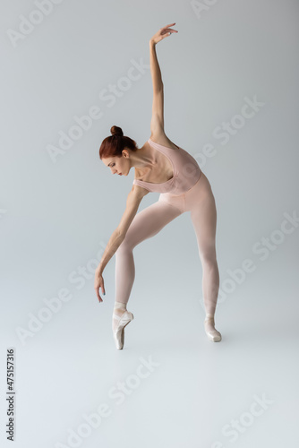 full length of ballerina in ballet shoes dancing with outstretched hand on grey