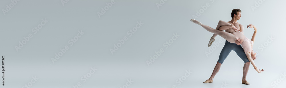 full length of elegant ballet dancers performing dance on grey, banner full length of elegant ballet dancers performing dance on grey, banner
