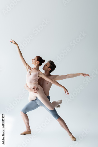 full length of shirtless man and flexible woman in bodysuit performing ballet dance on grey