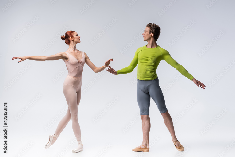 full length of young ballet dancer looking at graceful ballerina on grey