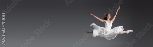 Billede på lærred full length of graceful woman in white dress jumping isolated on grey, banner