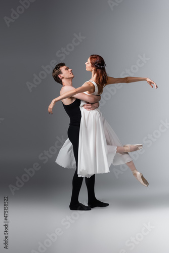 full length of man lifting graceful ballerina in white dress on dark grey