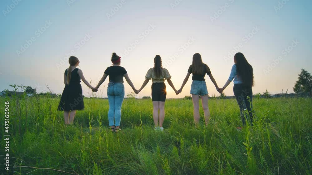 Girls friends go hand in hand at sunset across the field. Girls friends go hand in hand at sunset across the field.