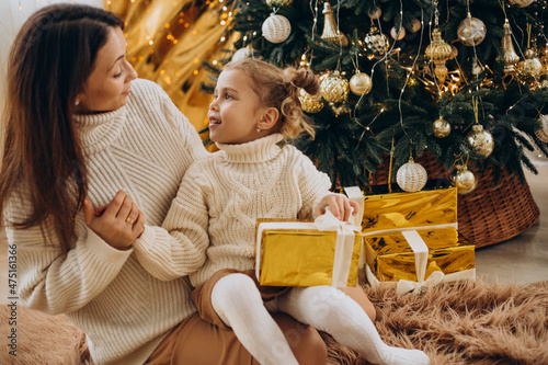 Mother with daughter holding christmas present under the christmas tree
