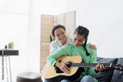 african american girl playing guitar while sitting on couch near mom