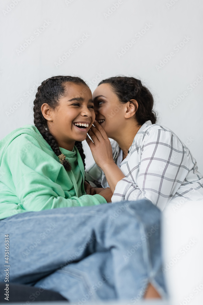 african american woman telling secret to cheerful daughter on blurred foreground african american woman telling secret to cheerful daughter on blurred foreground