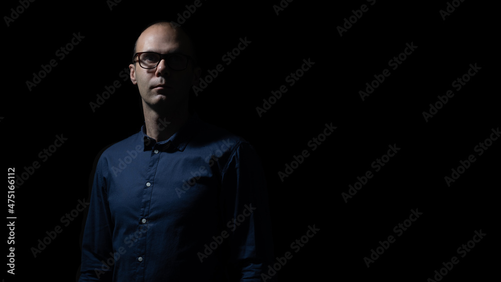 man in glasses and blue shirt  is staying in darkness, light and shadows on his face 
