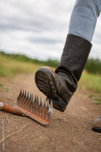 Step on the same rake. A man in kirza boots steps on a sharp metal rake. photo