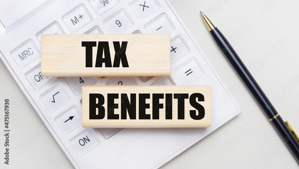 Wooden blocks with the TAX BENEFITS Iie on a light background on a white calculator. Nearby is a black handle. Business concept Wooden blocks with the TAX BENEFITS Iie on a light background on a white calculator. Nearby is a black handle. Business concept