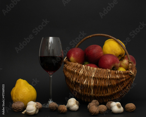 Vintage braided bascet with glass of red wine, apples, walnuts, garlic and apple quince  on black background. Traditional mediterranean  Christmas composition.