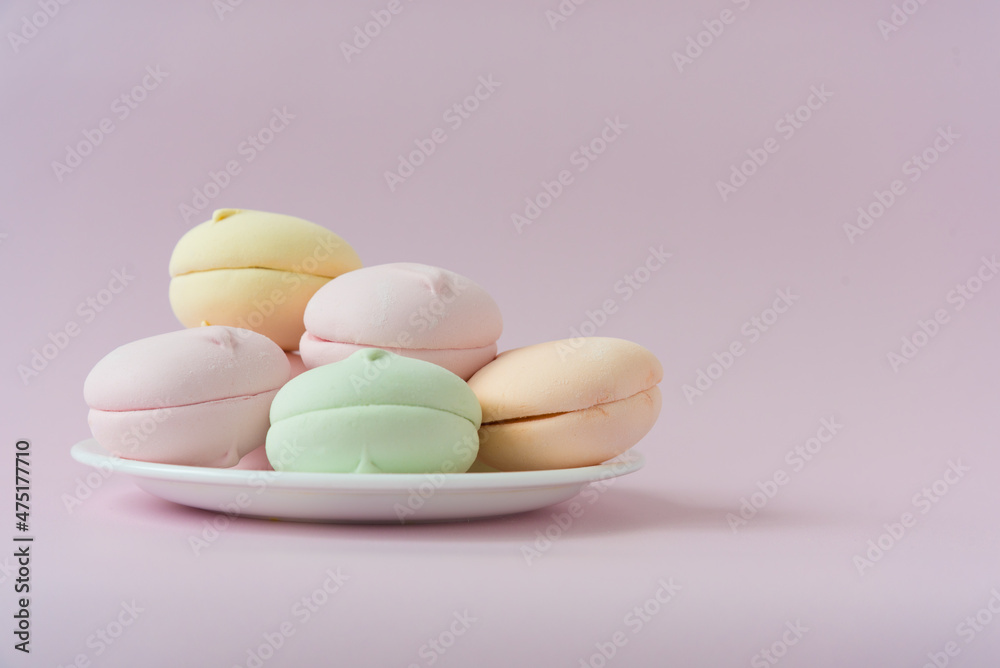 A multi-colored marshmallow lies on a saucer. Pink background. Free space for text A multi-colored marshmallow lies on a saucer. Pink background. Free space for text