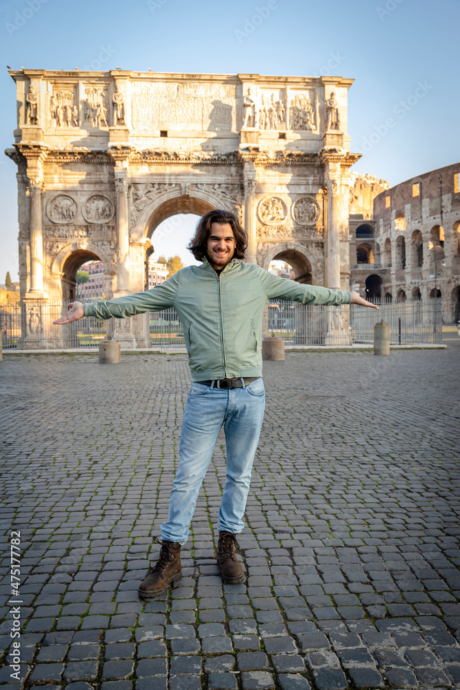 Happy moment in Rome. Young smiling man posing for a photo spreading his arms in front of the Arch of Titus.