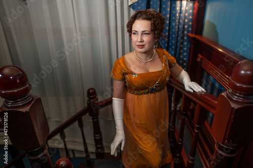 A woman in a 19th century dress climbs a wooden staircase in a hotel photo