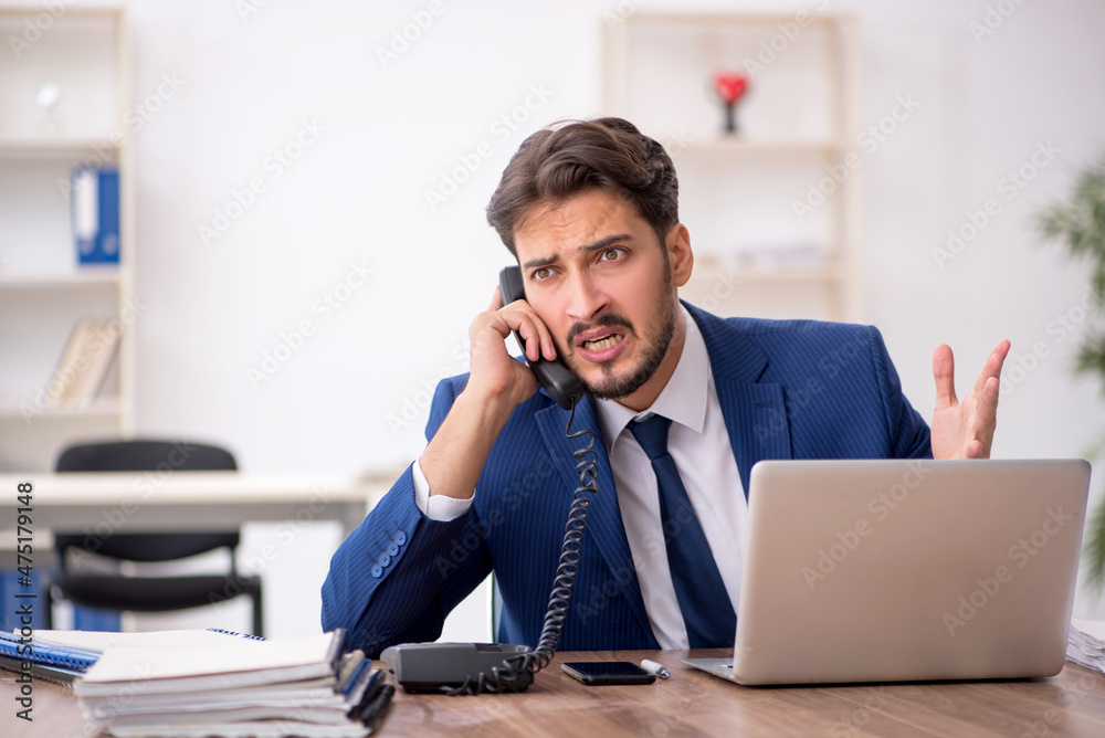Young male employee unhappy with excessive work in the office Young male employee unhappy with excessive work in the office