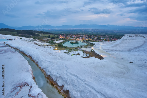 Pamukkale travertines in foreground. Sunset sky and illuminated houses