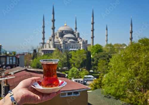Woman's hand holding cup with Traditional turkish tea in front of Blue mosque aka Sultanahmet Camii in Istanbul, Turkey.