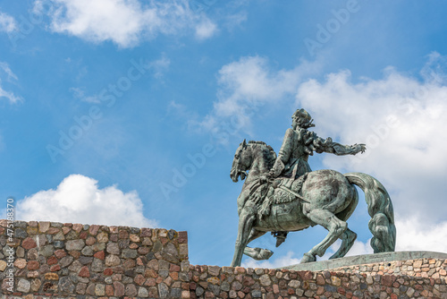 Bronze sculpture of a horseman on a horse on a stone pedestal.