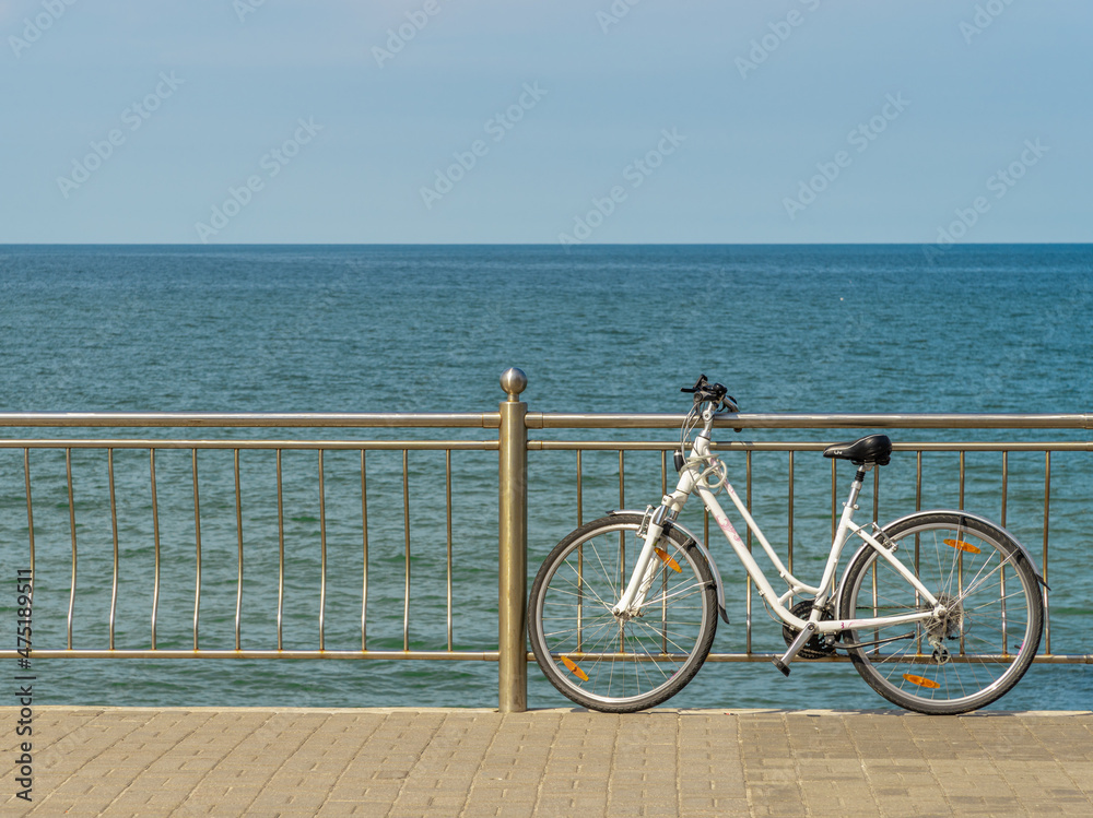 Fototapeta premium A lady's white bicycle standing at the railing against the background of the sea.