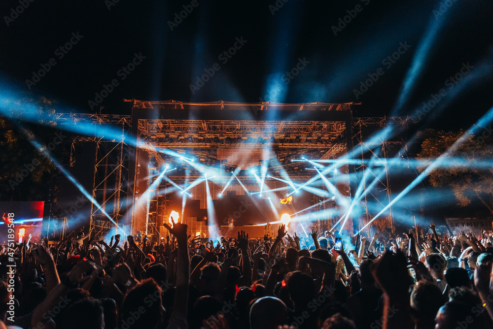 Silhouettes of concert crowd in front of bright stage lights on a music festival - obrazy, fototapety, plakaty 