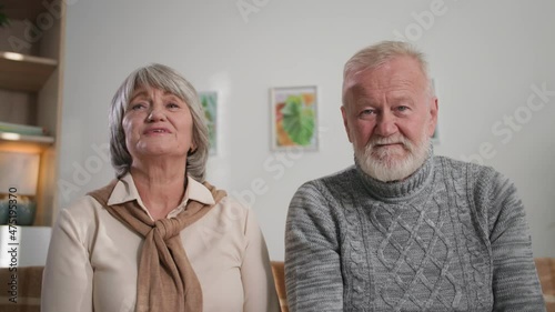 senior aged couple using laptop computer, smiling grandparents nod their heads together and waving hands on camera