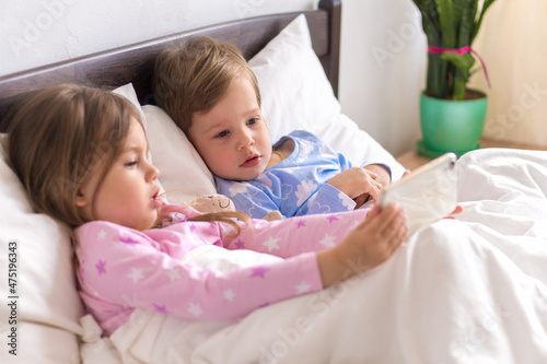 Little Preschool Toddler Minor Children Siblings Kids Watch Cartoon Use Smartphone Phone Device Together. Baby In Pajama On White Bed At Home Bedroom. Family, Leisure, Childhood, Friendship Concept