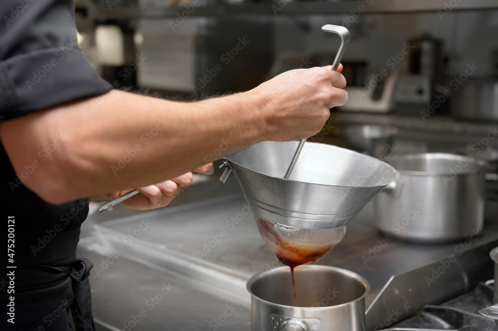 Cooking in the restaurant kitchen. Sifting sauce through a sieve. Chef is filtering sauce. High quality photo