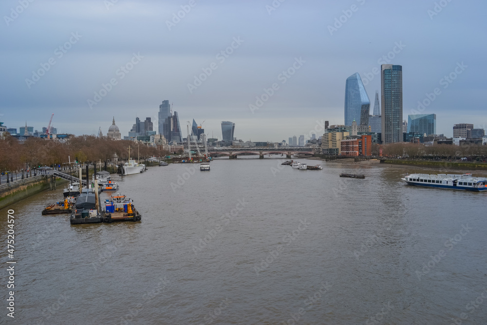 UK, London, 11.12.2021: A view of the Thames with ships, tall buildings in the background and a cloudy sky.