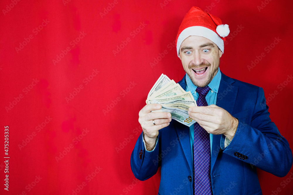 Happy businessman in santa hat with money on red background. Male entrepreneur in christmas hat holds dollar bills,New Year Lottery. Excited Guy In Santa Hat Holding Dollar Cash Happy businessman in santa hat with money on red background. Male entrepreneur in christmas hat holds dollar bills,New Year Lottery. Excited Guy In Santa Hat Holding Dollar Cash