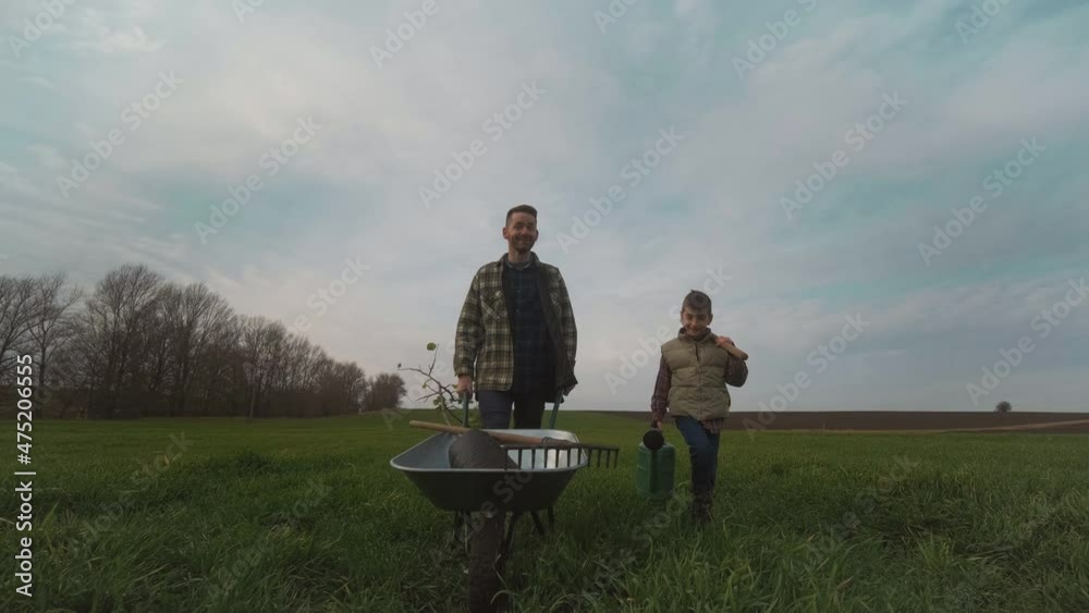 The dad and son walking through the field with a wheelbarrow. slow motion