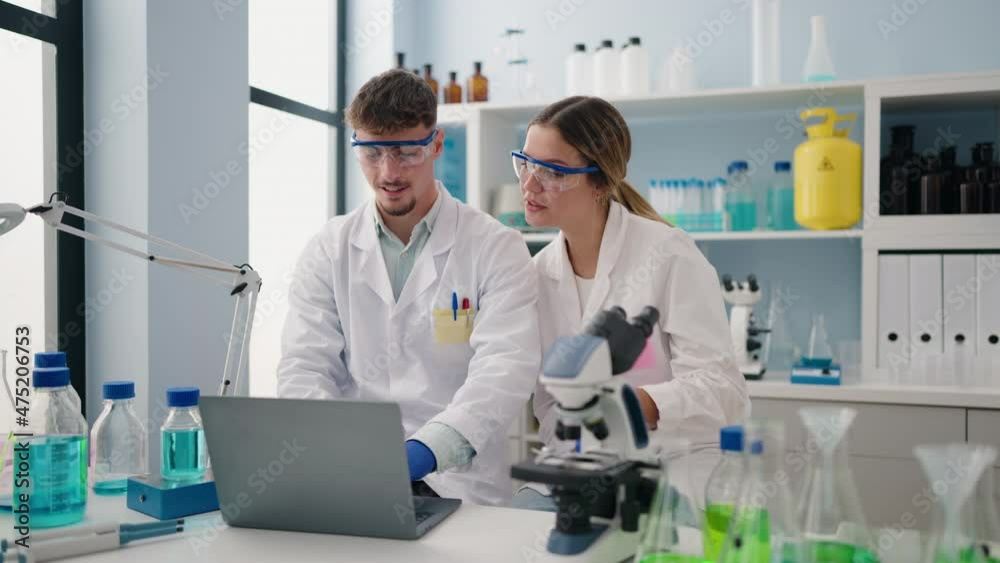 Young couple wearing scientist uniform using laptop at laboratory Young couple wearing scientist uniform using laptop at laboratory