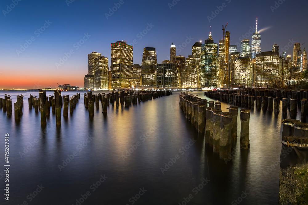 View of lower Manhattan at dusk seen from Brooklyn. Remaining of an old pier can be seen at the foreground and city skyline in the background