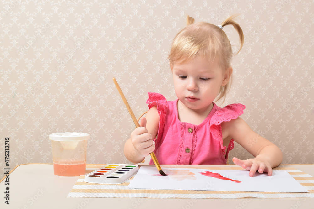 Cute little preschooler child drawing at home. A cute little preschool child in a pink suit paints houses with paints Cute little preschooler child drawing at home. A cute little preschool child in a pink suit paints houses with paints
