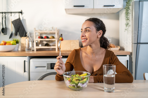 Latino attractive woman wear apron eat green salad in kitchen at home.