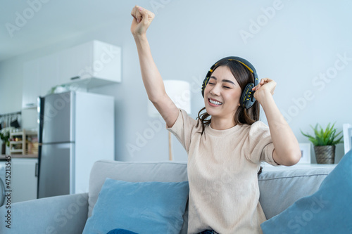 Asian funny woman listen to music and dance on floor in living room.