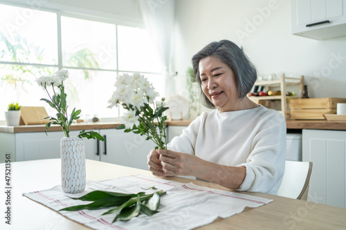 Asian senior old woman puts flowers on vase with happiness in kitchen.