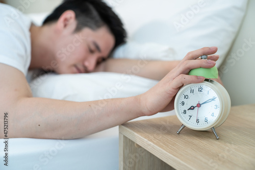 Asian attractive young man turn off alarm clock ringing in the morning