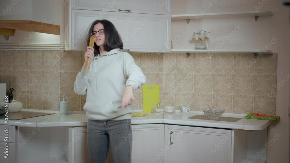 Girl teenager is having fun on the background of the kitchen at home, holding a wooden spoon and singing Girl teenager is having fun on the background of the kitchen at home, holding a wooden spoon and singing