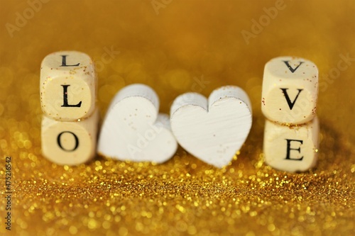 Love and relationship.Valentine's Day. Inscription love made of wooden letters and two hearts on a gold glitter background with gold bokeh. Valentines day background in gold tones.Love symbol