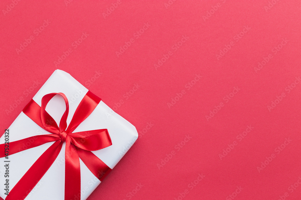 A small white gift with a red ribbon laying on a red background A small white gift with a red ribbon laying on a red background