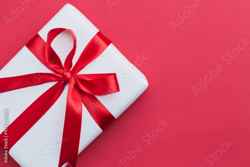 A small white gift with a red ribbon laying on a red background
