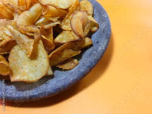 different angle an orange background of spicy domestic cassava chips on a stone mortar typical of the Indonesian people. Spicy cassava as Asian food. simple meal for hang out. 
