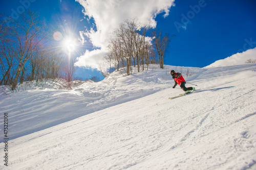 Skier wearing a mask riding down a groomed ski resort on a blue sky sunny day Hakuba Japan