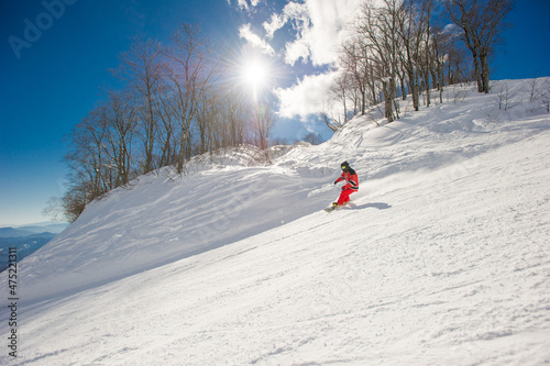 Snowboarder riding down a groomed ski resort on a blue sky sunny day Hakuba Japan