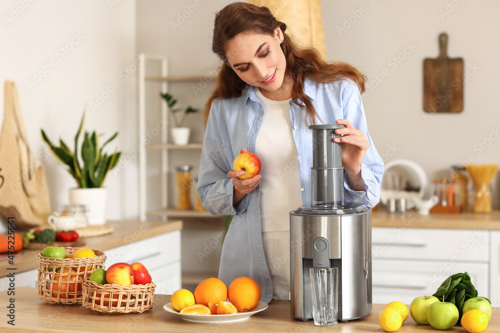 Young woman preparing healthy fruit juice in kitchen