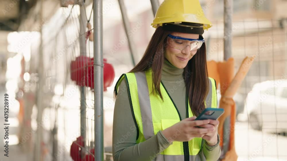 Young hispanic woman architect using smartphone at construction site