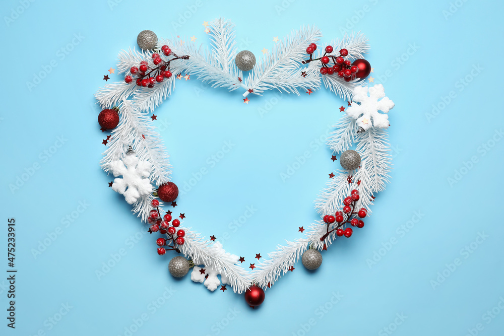 Heart made of white fir branches and Christmas decorations on blue background