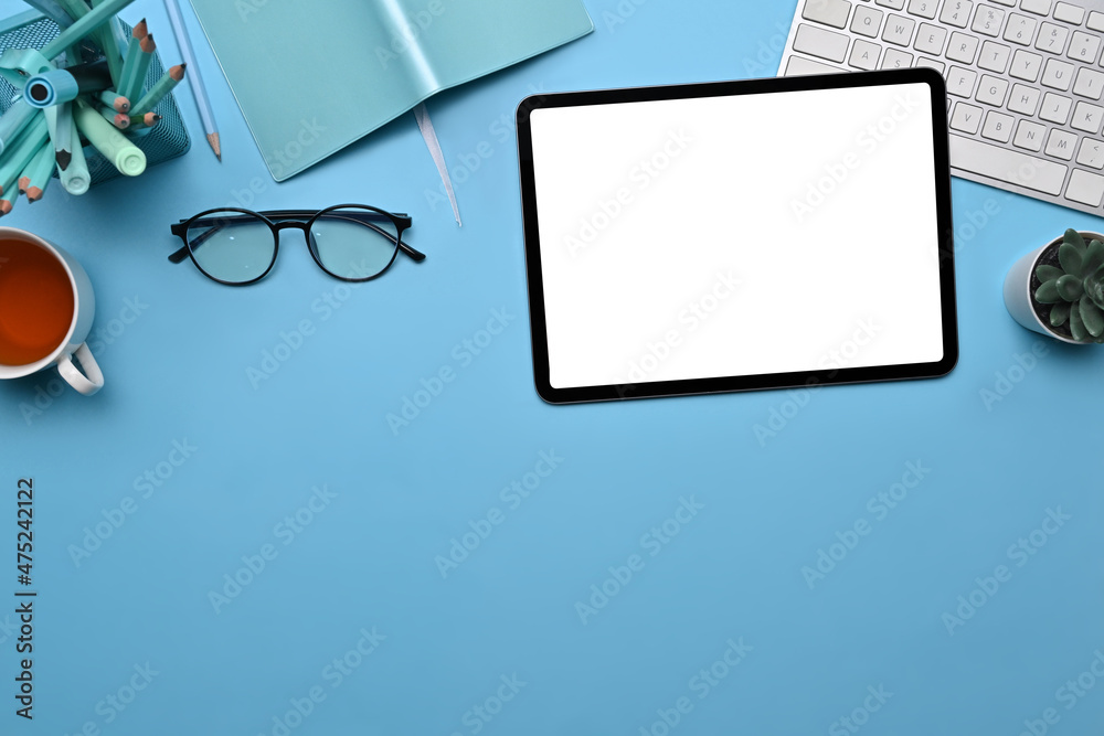 Top view stylish workspace with digital tablet, glasses, coffee cup and notebook on blue background.