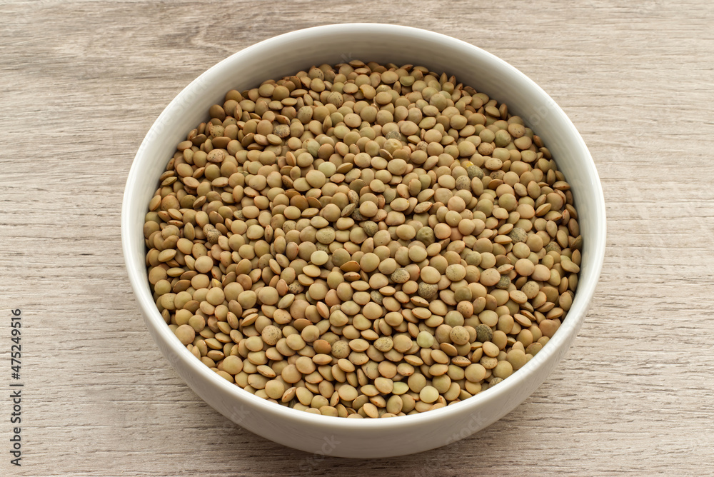 Uncooked Lentils in a bowl isolated on wooden background