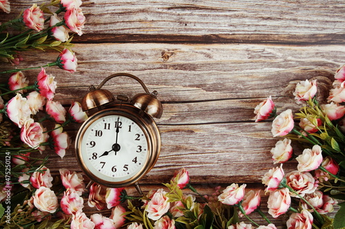 Alarm clock with Pink roses flowers border frame on wooden background